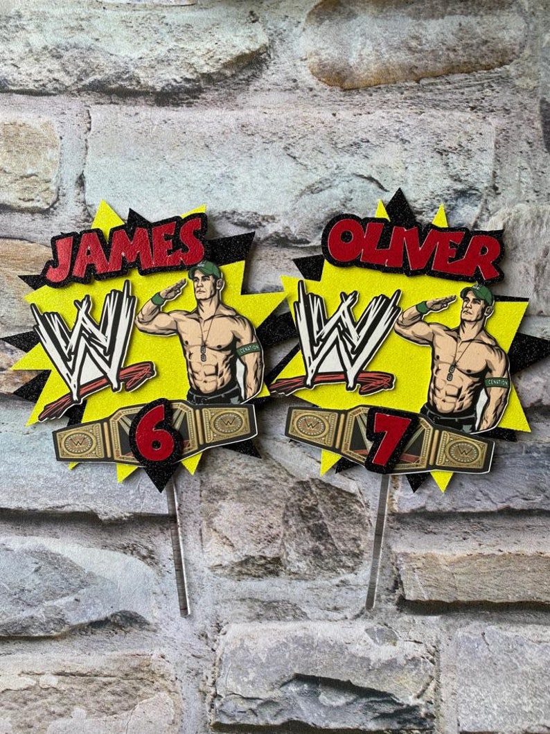 May include: Two WWE themed cake toppers featuring a wrestler with a championship belt. The toppers are yellow and black with the wrestler's name, "JAMES" and "OLIVER", in red. The numbers "6" and "7" are also included on the toppers.