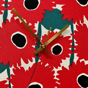 Könnte beinhalten: Eine goldene Uhr mit schwarzen Zeigern vor einem roten und grünen floralen Hintergrund. Das Zifferblatt der Uhr ist mit einem roten und weißen Blumenmuster bedeckt.
