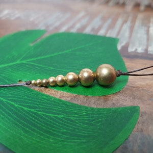 May include: A gold beaded necklace with a brown cord and a tassel. The beads are graduated in size, with the largest bead at the end of the necklace.