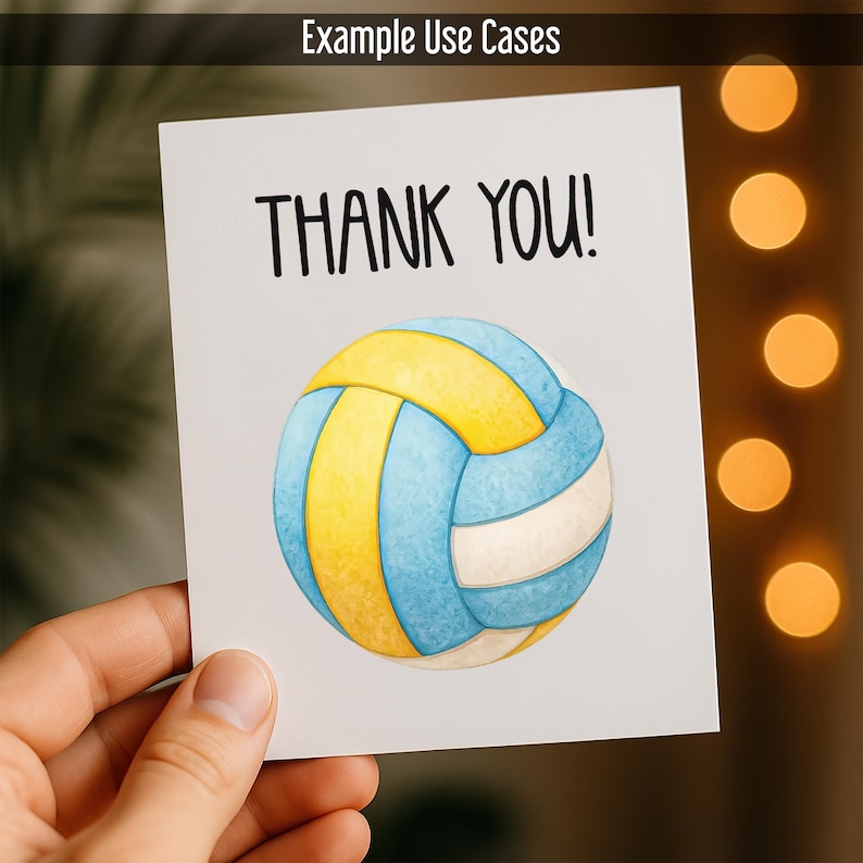 May include: A white card with the text "THANK YOU!" in black, featuring a watercolour illustration of a volleyball in blue, yellow, and white. The card is held by a hand, with a blurred background.