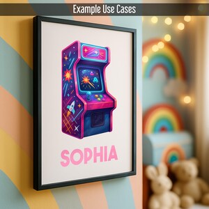 May include: Framed print with a vibrant arcade game illustration. The artwork depicts a retro arcade machine in pinks, purples, and blues, with a rocket and stars. The name "SOPHIA" is printed in pink below the arcade game.