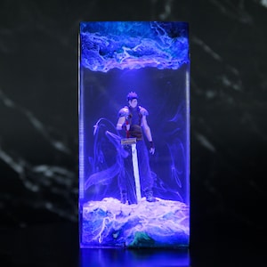 May include: A rectangular resin art piece featuring a figure with a sword, set against a blue, cloud-like background. The figure is in a fighting stance, with a sword held upright. The resin is clear, allowing the figure to be seen.
