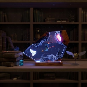 May include: A decorative resin lamp featuring a wizard flying on a broomstick, set against a starry night sky and rocky landscape. The lamp has a wooden base and is illuminated with a soft glow, with a golden snitch figurine nearby.