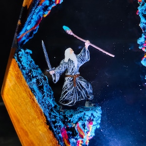 May include: A miniature wizard figure with a sword and staff, set within a resin art piece. The artwork features vibrant blue, orange, and red accents, creating a fantasy scene. The wizard is dressed in a gray robe with a brown belt.