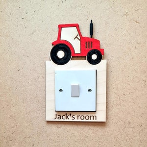 May include: A wooden light switch cover with a red tractor design. The tractor is above a white light switch and a wooden frame with the text "Jack's room".
