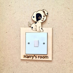 May include: A wooden light switch cover with a cartoon Dalmatian dog on top. The cover has a white light switch and the text "Harry's room" is engraved below the switch.