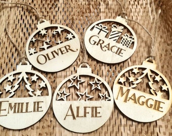 May include: Five wooden Christmas ornaments with names "Oliver", "Gracie", "Emillie", "Alfie", and "Maggie" engraved on them. Each ornament features a different design, including stars, a Christmas tree, and gift boxes.