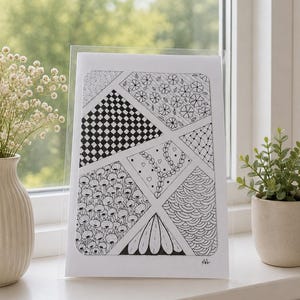 May include: Black and white geometric art print in a clear acrylic frame. The artwork features various patterns, including checkerboard, floral, and wave designs. The print is displayed on a white windowsill with a vase of white flowers and a potted plant.