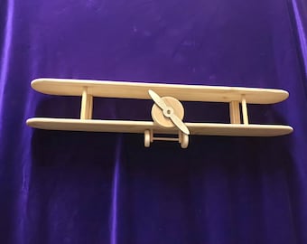 May include: A wooden toy airplane with a propeller. The airplane is painted in a natural wood color.