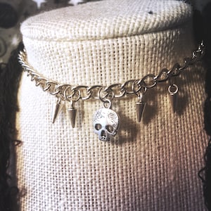 May include: Silver chain choker necklace with a skull charm and multiple silver spike charms.