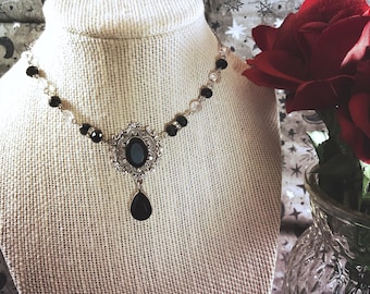 May include: A black and silver choker necklace with a large black gemstone pendant. The necklace is on a white mannequin bust against a background of silver stars.