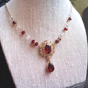May include: A gold necklace with a large red gemstone pendant and smaller red gemstones along the chain. The pendant is ornate and features a teardrop-shaped gemstone.