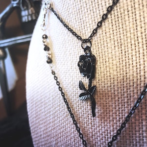 May include: A layered necklace with a black rose pendant. The necklace is made of two chains, one silver and one black.