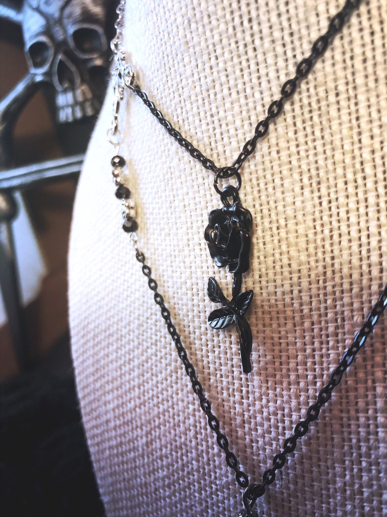 May include: A layered necklace with a black rose pendant. The necklace is made of two chains, one silver and one black.