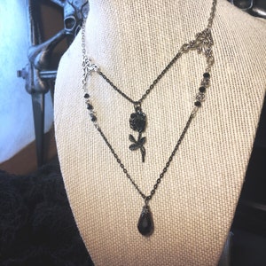 May include: A layered black and silver necklace with a black rose pendant and a teardrop-shaped black crystal pendant.
