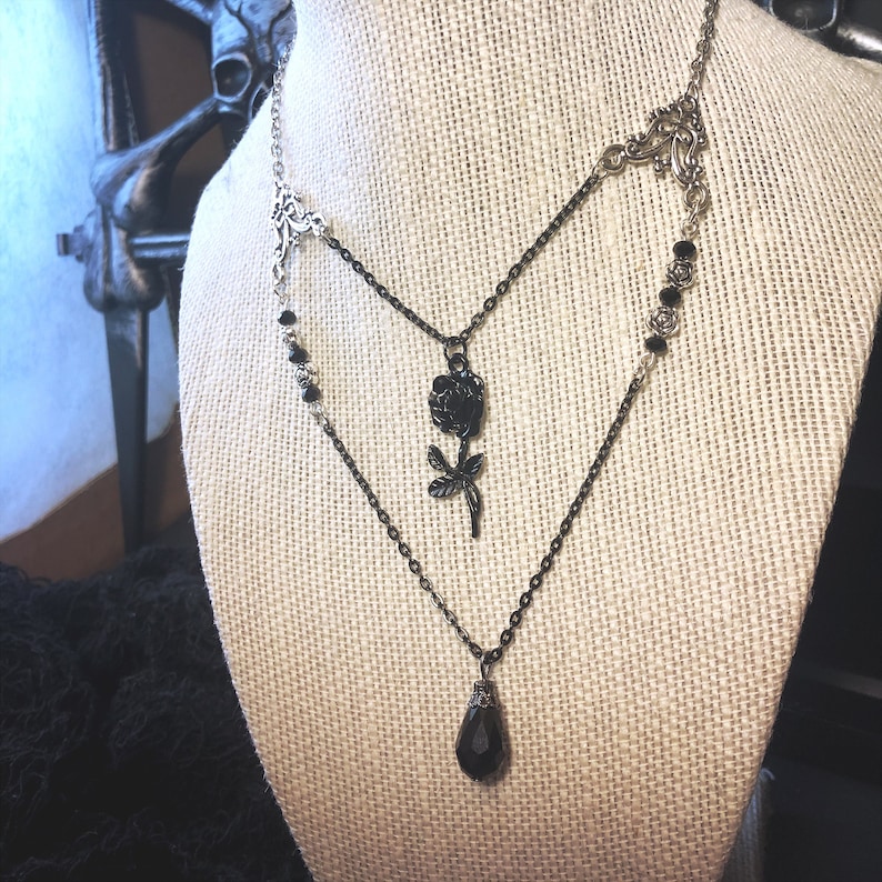 May include: A layered black and silver necklace with a black rose pendant and a teardrop-shaped black crystal pendant.