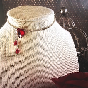 May include: A silver chain choker necklace with a dangling red heart-shaped crystal and two smaller red crystal drops.