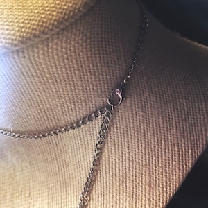 Pu&ograve; includere: Una collana a catena d'argento con chiusura a moschettone. La catena &egrave; su un manichino rivestito in tessuto.
