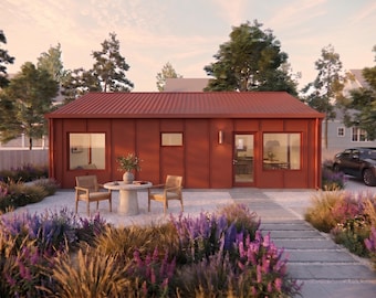May include: A single-story house with a rust-colored metal exterior, a gabled roof, and large windows. In front, a round concrete table is flanked by two wooden chairs with woven seats, set upon a gravel patio surrounded by purple flowering plants.