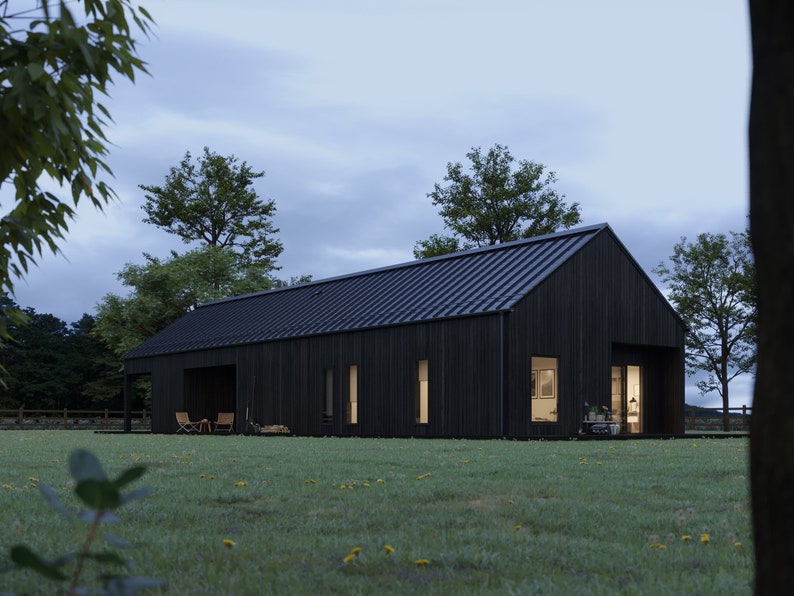 May include: A modern, black-clad house with a dark metal roof sits on a grassy lawn. The house has large windows and a covered porch area. Trees and a fence are visible in the background, under a cloudy sky.
