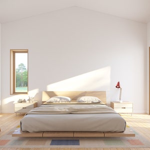 May include: A minimalist bedroom with a light wood bed frame, two bedside tables, and a wooden chair. The bed is covered with a beige comforter and pillows. A red desk lamp sits on one of the bedside tables. A large window and a smaller window provide natural light.