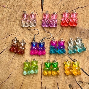 Könnte beinhalten: Ein Set mit 10 Paaren Gummibärchen-Ohrringen in verschiedenen Farben, darunter Pink, Lila, Rot, Orange, Blau, Grün und Gelb. Jedes Paar besteht aus zwei Gummibärchen mit einem Farbverlaufseffekt.