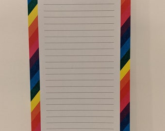 Op de afbeelding: Een wit notitieboekje met een regenboogrand en de tekst "Het is een goede dag om gelukkig te zijn".