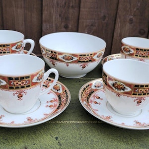May include: A vintage tea set comprising white teacups and saucers with an orange, brown, and black patterned border, plus a serving bowl. The set is displayed on a green surface.
