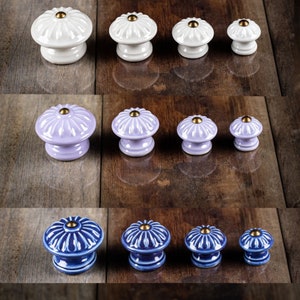 Peut inclure: Ensemble de boutons de meubles en céramique blancs, lavande et bleus. Chaque bouton présente un design cannelé et un centre doré. Les boutons sont disposés en rangées, présentant différentes tailles, parfaits pour les meubles.