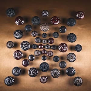 May include: A collection of ceramic knobs in various shades of brown, black, and gray. The knobs have a unique, swirling design and are arranged in a circular pattern on a brown background.