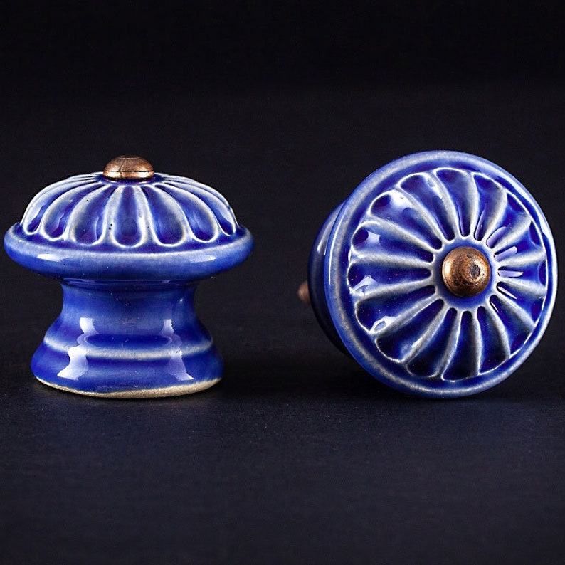 May include: Two blue ceramic cabinet knobs with a raised floral design and a copper center.