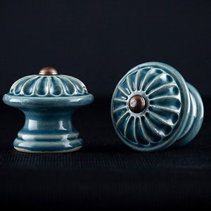 May include: Two ceramic cabinet knobs with a blue glaze and a copper center. The knobs have a floral design.