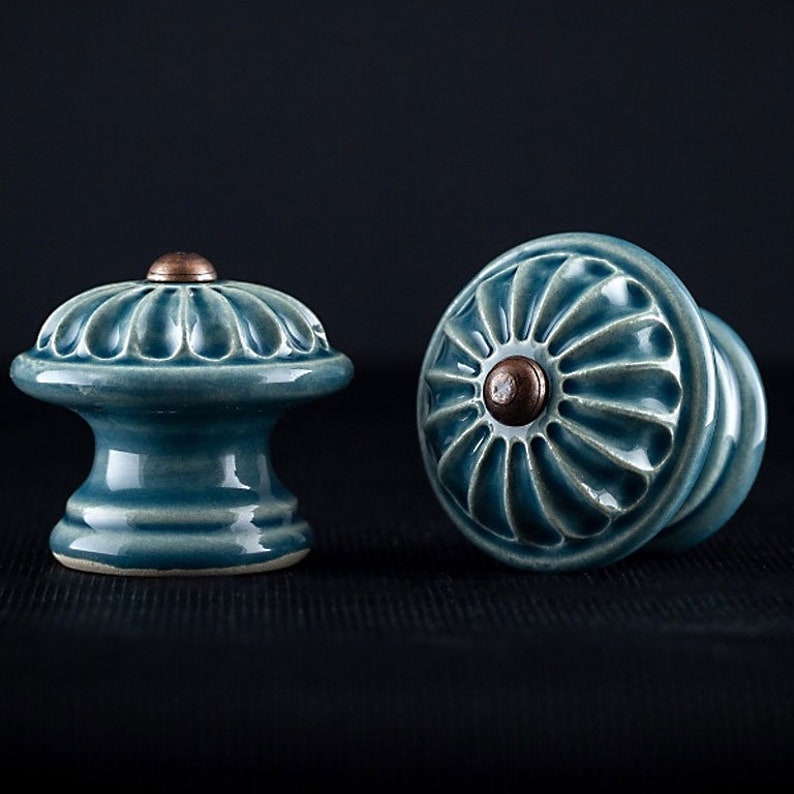 May include: Two ceramic cabinet knobs with a blue glaze and a copper center. The knobs have a floral design.
