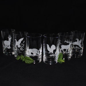 Puede incluir: Seis vasos transparentes de vidrio con diseños grabados de varios animales, incluyendo un ciervo, un pájaro, un jabalí, un gallo y un faisán. Los vasos están dispuestos en una fila sobre una superficie negra.