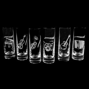 May include: Six clear glass shot glasses with different musical instruments etched on them. The instruments include a piano, violin, trumpet, drum set, guitar, and accordion.