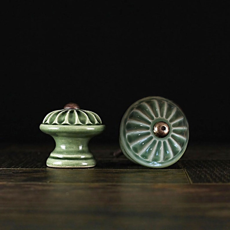 May include: Two green ceramic cabinet knobs with a raised, fluted design. One knob is round and the other is a traditional knob shape.