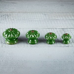 May include: Four green ceramic knobs with a floral design and gold accents. The knobs are arranged in a row from largest to smallest.