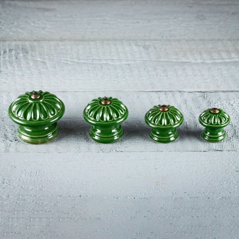 May include: Four green ceramic knobs with a floral design and gold accents. The knobs are arranged in a row from largest to smallest.