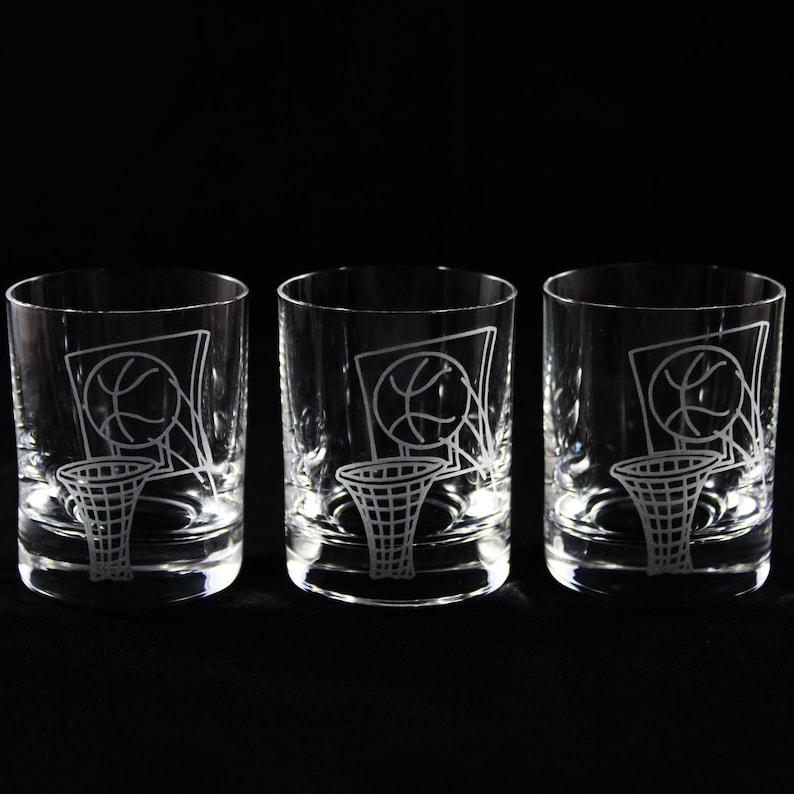 May include: Three clear, lowball glasses with etched basketball hoop and ball designs. The glasses are cylindrical with a thick base, perfect for serving cocktails or other beverages. The basketball theme is visible on each glass.