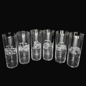 May include: A set of six clear glass tumblers, each decorated with a white etched design of a tractor. The glasses are tall and cylindrical, suitable for various beverages. Each glass has a different tractor design.