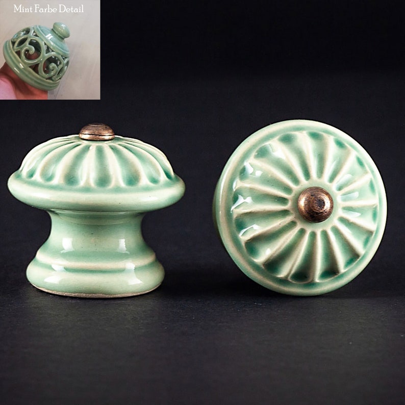 May include: Two ceramic cabinet knobs in a light green color with a raised, textured design. One knob has a round shape with a raised center, while the other has a round top with a raised, cylindrical base. Both knobs have a brass colored center.