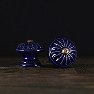 May include: Two blue ceramic cabinet knobs with a decorative floral design. The knobs have a raised center with a copper-colored accent.