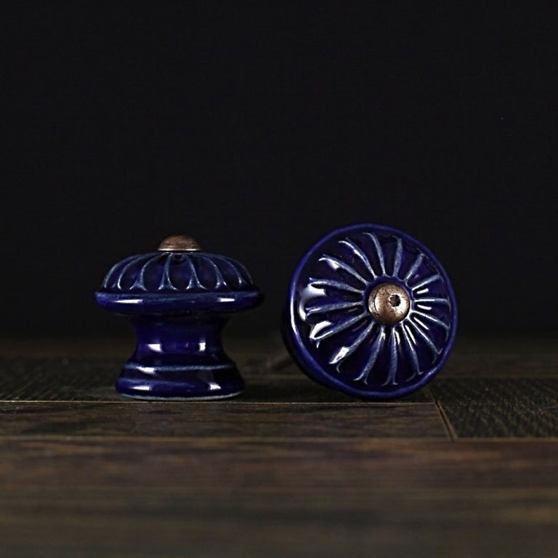 May include: Two blue ceramic cabinet knobs with a decorative floral design. The knobs have a raised center with a copper-colored accent.