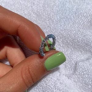 Puede incluir: Un anillo de plata con un diseño de cuentas. El anillo está sostenido por una mano con esmalte de uñas verde.