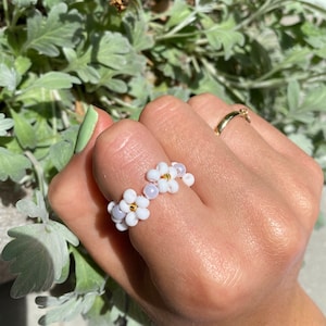 May include: White beaded ring with a flower design. The ring is made of small white beads and has a delicate floral pattern.