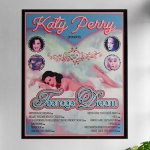 May include: A framed poster for Katy Perry's "Teenage Dream" album, featuring the album title in a stylized font. The poster includes images of Katy Perry and a list of songs. The poster is displayed on a white wall.