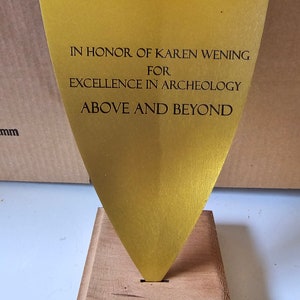 May include: A gold-colored award plaque with the inscription "In honor of Karen Wening for excellence in archeology above and beyond."