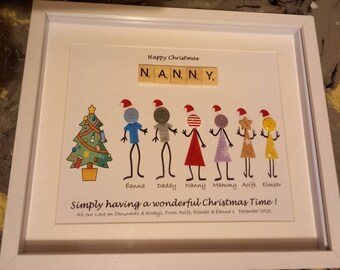 May include: A framed Christmas-themed artwork featuring a decorated Christmas tree and stick figures of a family with the word "NANNY" spelled out in Scrabble tiles. The text below reads "Simply having a wonderful Christmas Time! All our Love on Christmas & always, From Aoife, Eimear & Éanna x December 2021."
