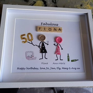 Könnte beinhalten: Ein weiß gerahmtes Bild mit weißem Hintergrund. Das Bild zeigt eine goldene Zahl 50, das Wort "Fabulous" mit Buchstabenkacheln ausgeschrieben und zwei Strichmännchen mit Knopfgesichtern. Die Strichmännchen halten Weingläser in der Hand. Der Text "Happy birthday, love Jo, Jan, Elz, Meez & Anz xx" befindet sich am unteren Rand des Bildes.
