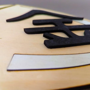 May include: Close-up of a wooden sign with the Japanese character for "gold" written in black.